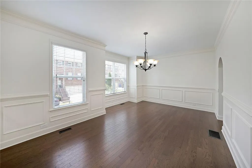 Unfurnished dining area with a chandelier, dark wood finished floors, a decorative wall, a wainscoted wall, and arched walkways