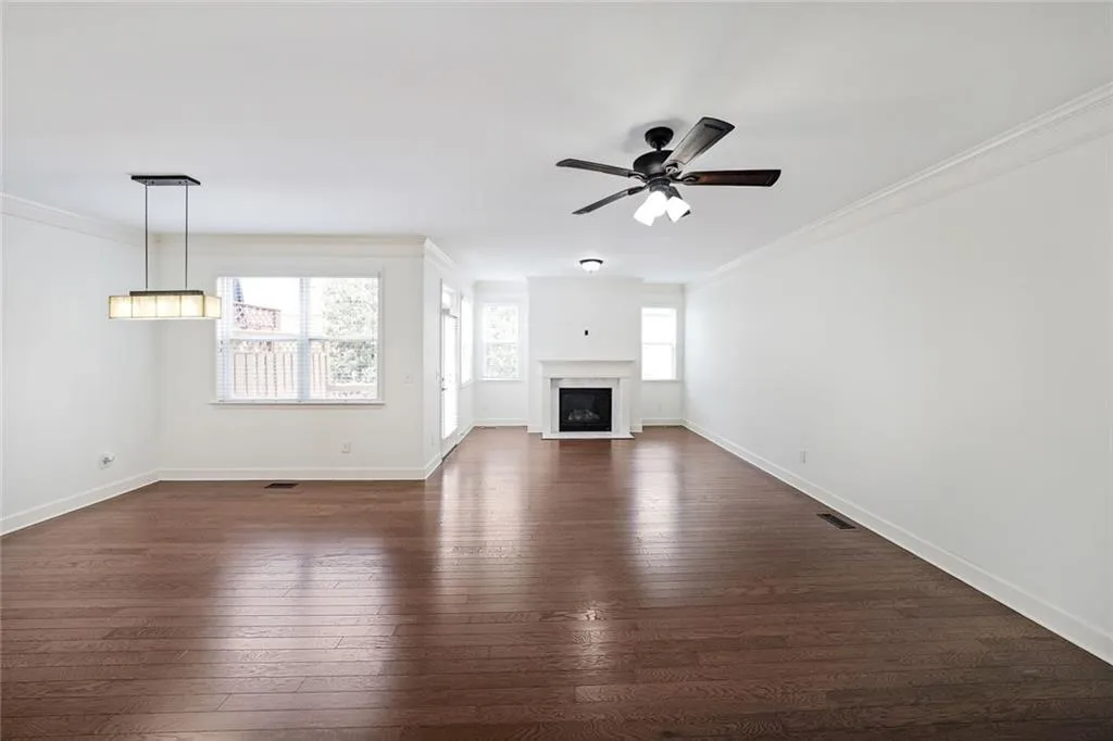 Unfurnished living room featuring ornamental molding, a ceiling fan, dark wood-style flooring, and a fireplace