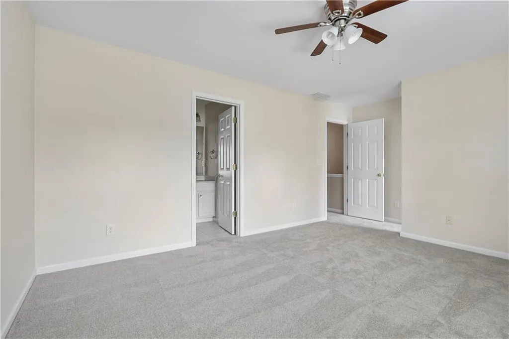 Unfurnished bedroom with baseboards, ensuite bathroom, carpet, and a ceiling fan
