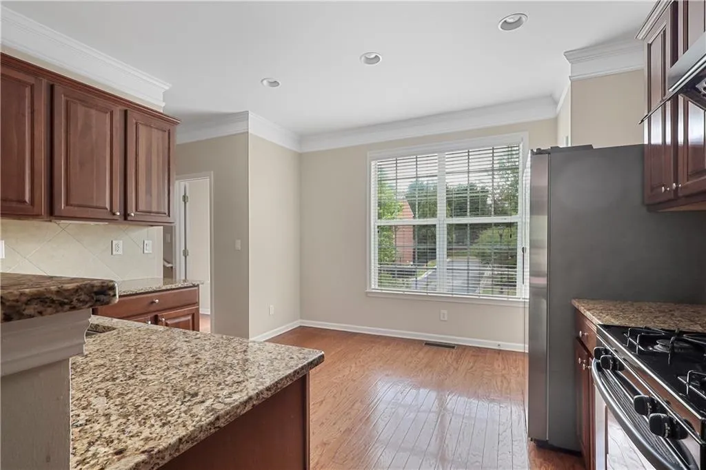 Kitchen with light stone counters, tasteful backsplash, ornamental molding, and hardwood / wood-style flooring