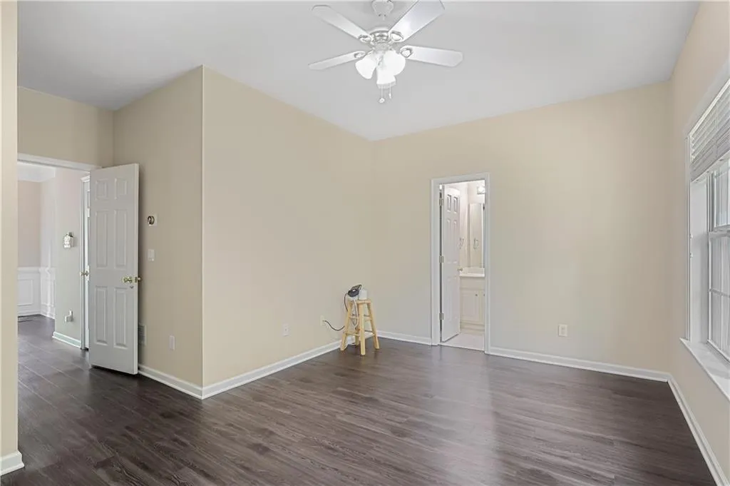 Unfurnished bedroom with dark wood-type flooring, baseboards, ensuite bathroom, and ceiling fan