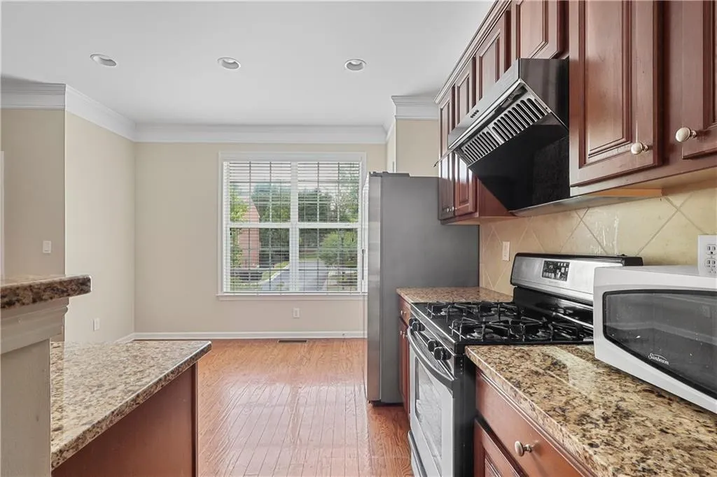 Kitchen with under cabinet range hood, crown molding, light wood-style flooring, and gas range