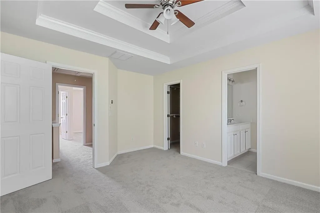 Unfurnished bedroom with a tray ceiling, crown molding, attic access, and light colored carpet