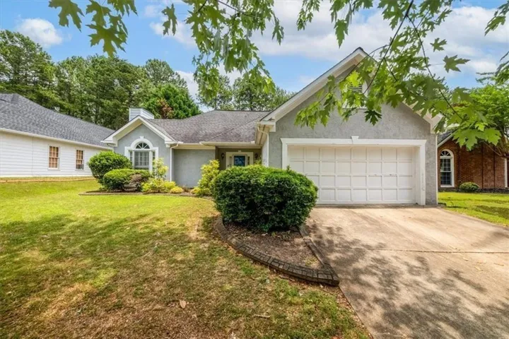 Stucco exterior with an attached garage, arched window, and mature landscaping