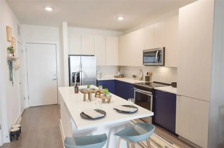 Kitchen featuring blue cabinets, light hardwood / wood-style flooring, white cabinetry, stainless steel appliances, and a center island with sink