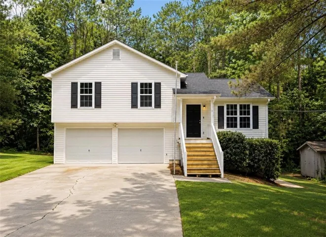 Split-level residence featuring white siding, black shutters, a covered entry with wood stairs, and an attached two-car garage