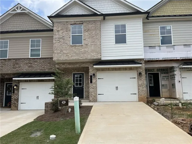 Brick and siding townhome exterior featuring a single-car garage, black front door with glass panes, and an awning