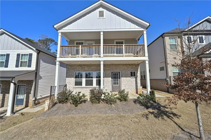Two-story dwelling with a ground-level entrance, covered upper-level balcony with wood railing, and brick-finish siding on the lower level