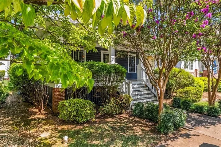 Exterior featuring dark siding, white trim, a porch with white railings, and mature trees with lush foliage