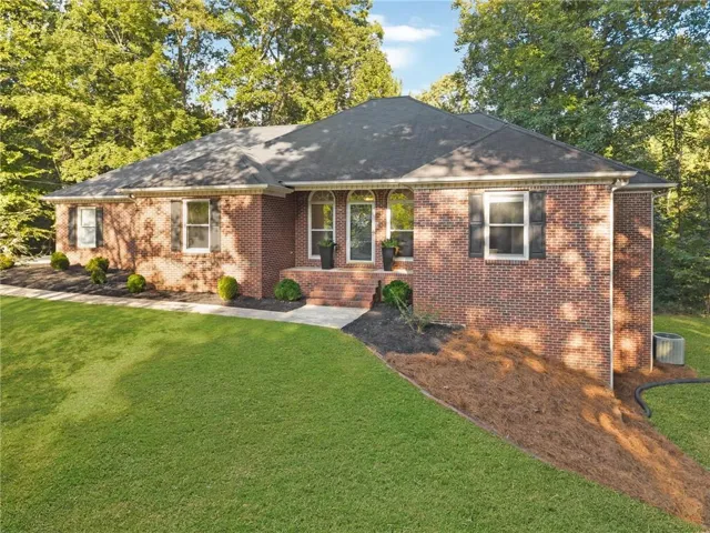 Brick exterior construction with an arched entry, a dark shingle roof, and a manicured lawn