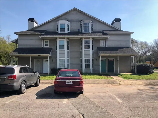 View of front facade featuring a chimney, roof with shingles, and uncovered parking