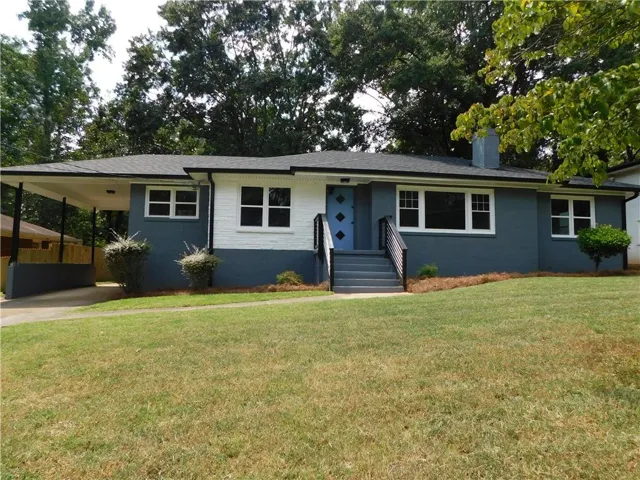 Exterior featuring a carport, a prominent chimney, concrete steps with dark railings, a light blue front door, and a well-maintained lawn