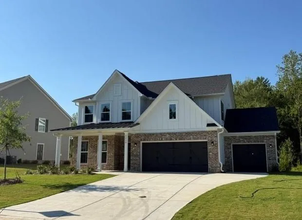 Stately residence featuring a brick and board-and-batten facade, covered front porch, multiple gables, and an attached two-car garage with an additional single-car garage