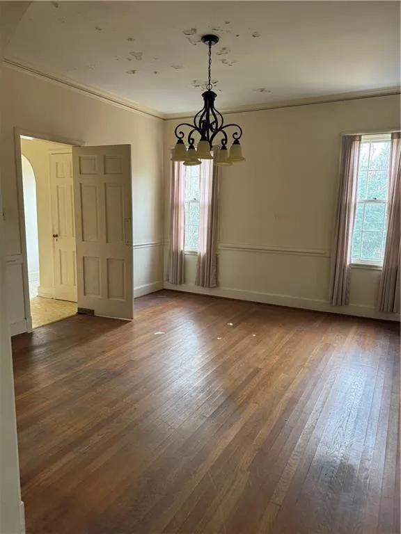 Empty room with arched walkways, hardwood / wood-style floors, ornamental molding, and a chandelier