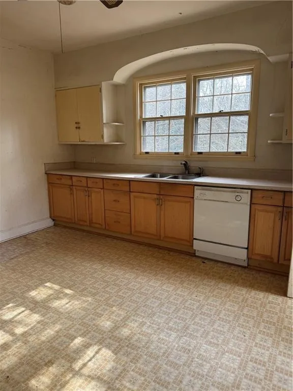 Kitchen featuring open shelves, dishwasher, light countertops, and brown cabinetry