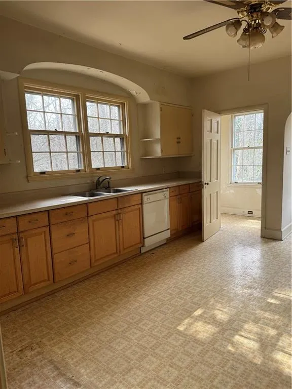 Kitchen featuring light countertops, ceiling fan, dishwashing machine, arched walkways, and light floors