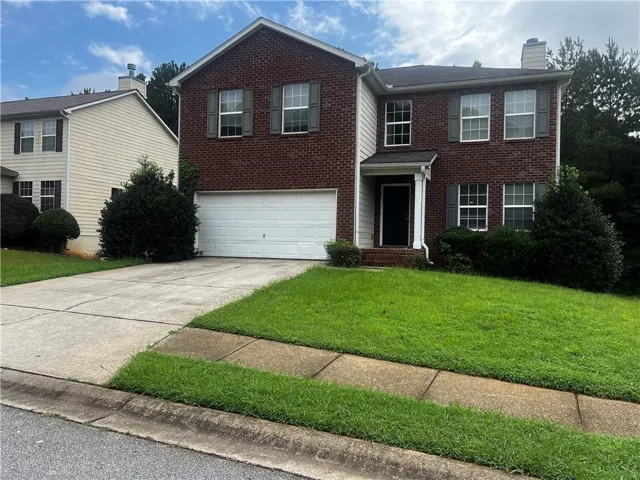 Brick facade home featuring a two-story design, an attached garage, a covered entryway, and mature landscaping