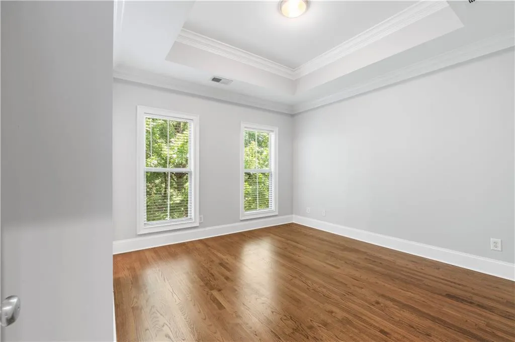 Empty room featuring a tray ceiling, dark wood-style flooring, baseboards, and ornamental molding