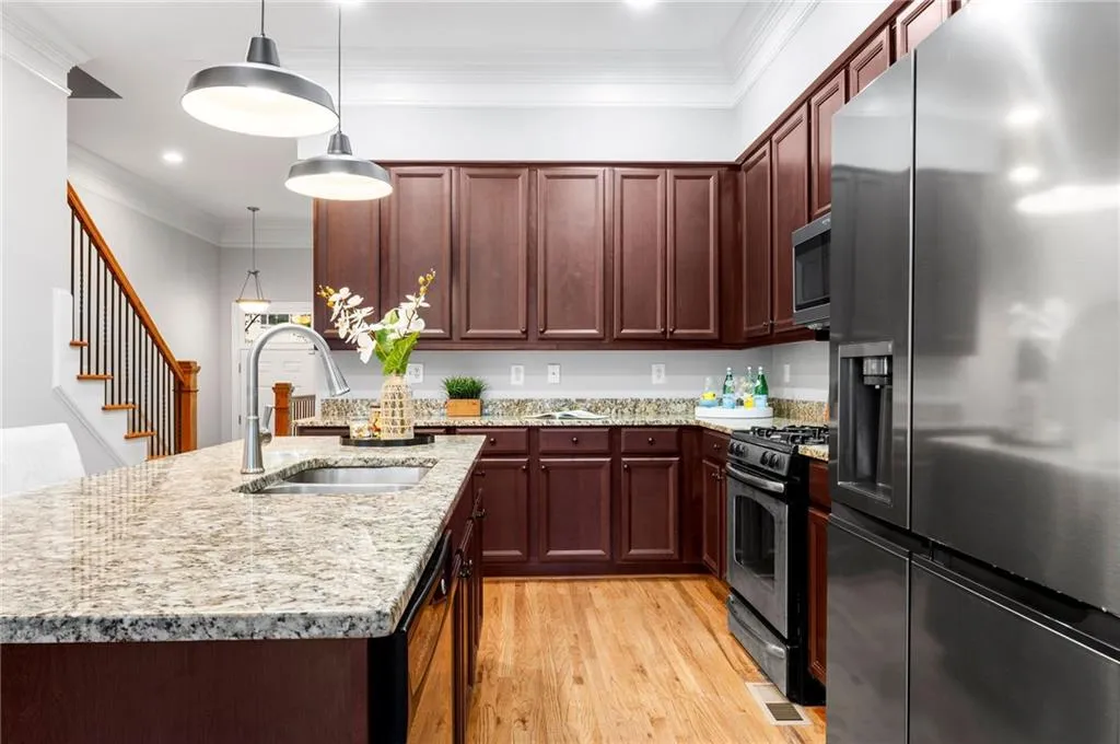 Kitchen with stainless steel appliances, a sink, light wood-style floors, hanging light fixtures, and ornamental molding