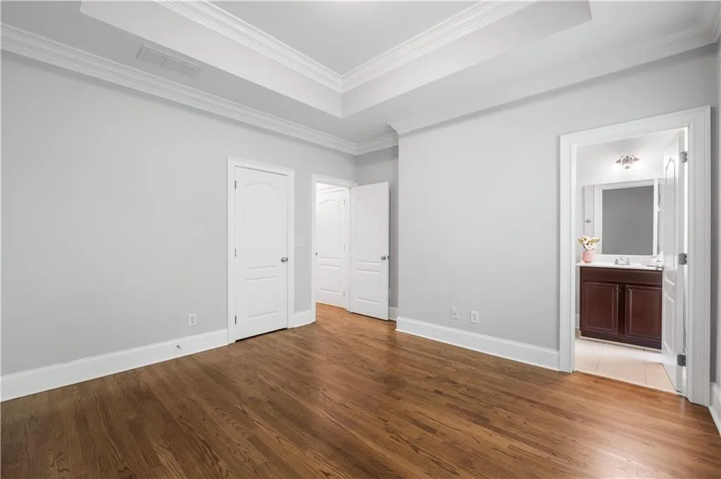 Unfurnished bedroom with wood finished floors, crown molding, baseboards, and a tray ceiling