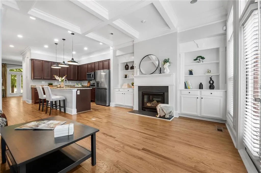 Living area featuring crown molding, beam ceiling, a glass covered fireplace, light wood finished floors, and recessed lighting