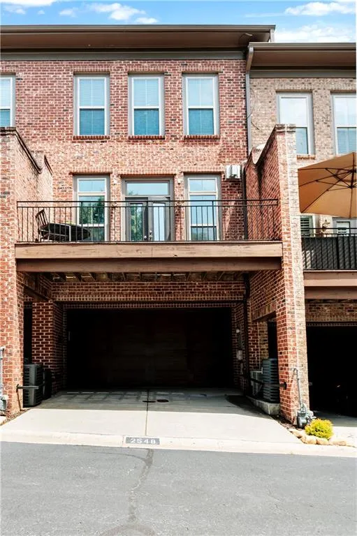 Rear view of property with brick siding, a garage, driveway, and central AC unit