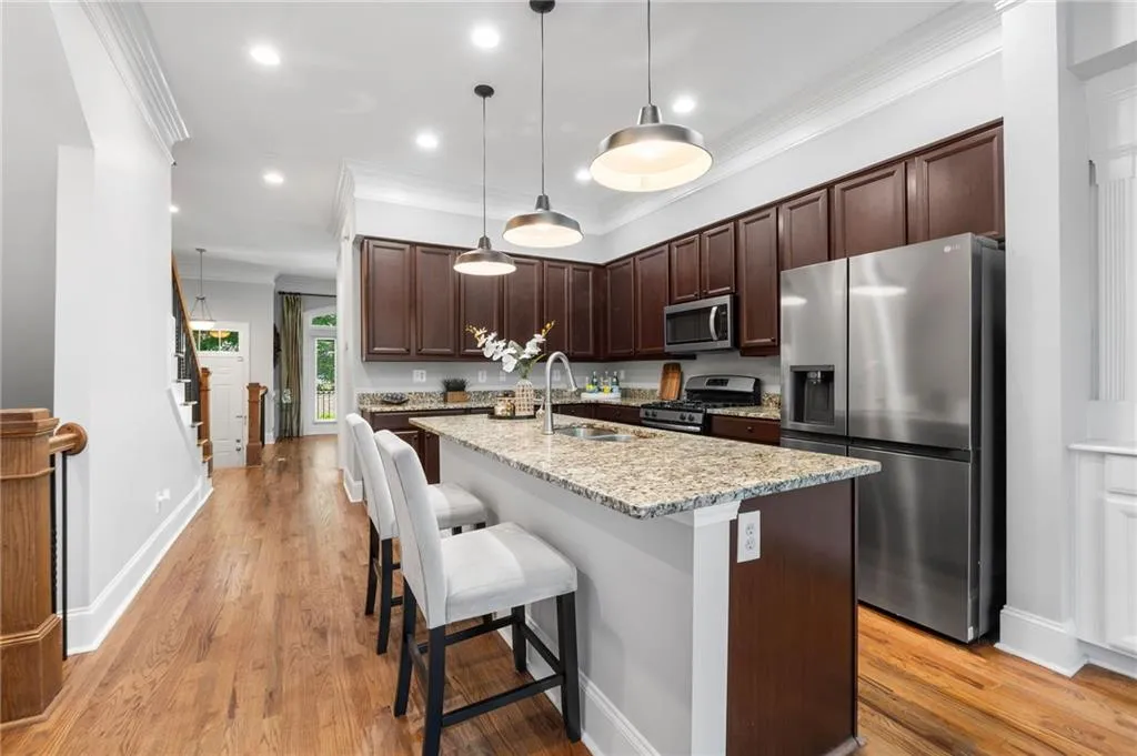 Kitchen with stainless steel appliances, a sink, dark brown cabinets, ornamental molding, and a kitchen island with sink