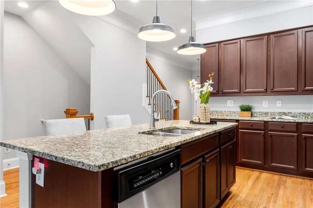 Kitchen featuring a sink, dishwasher, light wood-style floors, ornamental molding, and a center island with sink