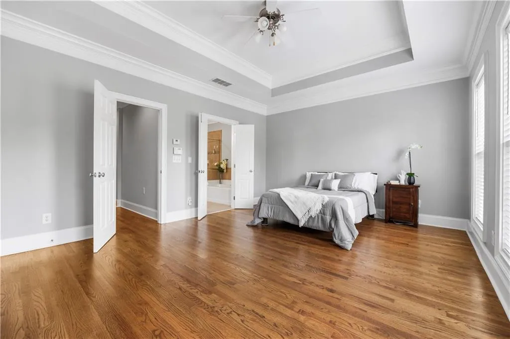 Bedroom featuring wood finished floors, a tray ceiling, baseboards, and crown molding