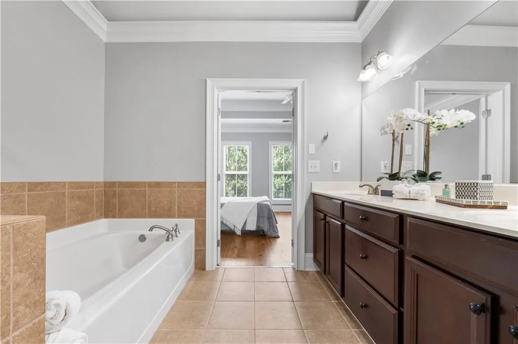Ensuite bathroom featuring ornamental molding, double vanity, a garden tub, and tile patterned flooring