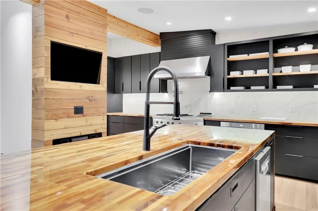 Kitchen featuring backsplash, dark cabinets, modern cabinets, light wood-style flooring, and stainless steel dishwasher