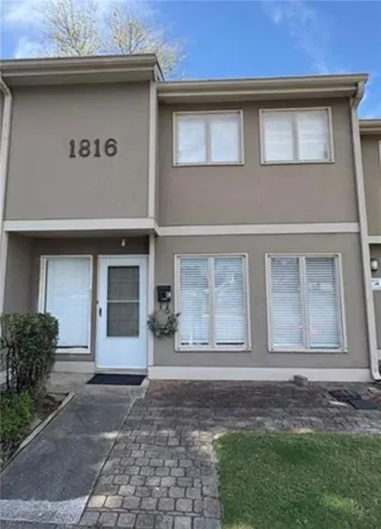 Stucco exterior with multiple windows, a white front door, and a paver walkway