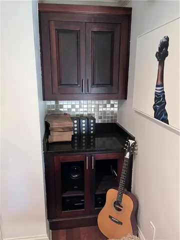 Bar with dark brown cabinetry, tasteful backsplash, dark countertops, and wood finished floors