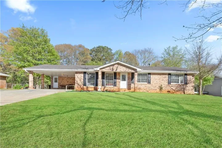 Photos showing the lawn have been digitally enhanced to illustrate potential landscaping appearance. Brick exterior with white trim, covered carport, black window shutters, and a front entry door