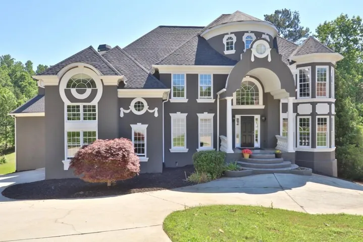 Stately stucco exterior with extensive white trim, a turreted architectural feature, arched entryway, bay windows, and a curved driveway