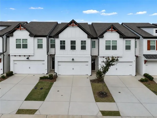 Modern townhome featuring white brick and siding exterior, dark shingle roof, integrated single-car garage, and concrete driveway