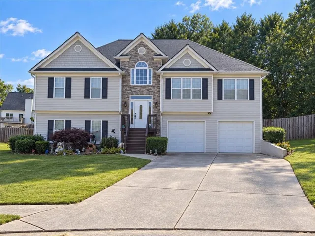 Two-story residence featuring light gray siding, stone facade accents, and a dual garage