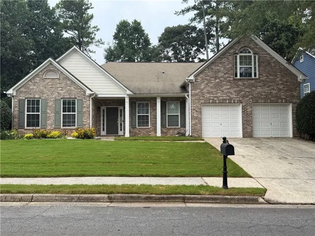 Brick-front residence featuring a two-car garage, mature trees, and a concrete driveway