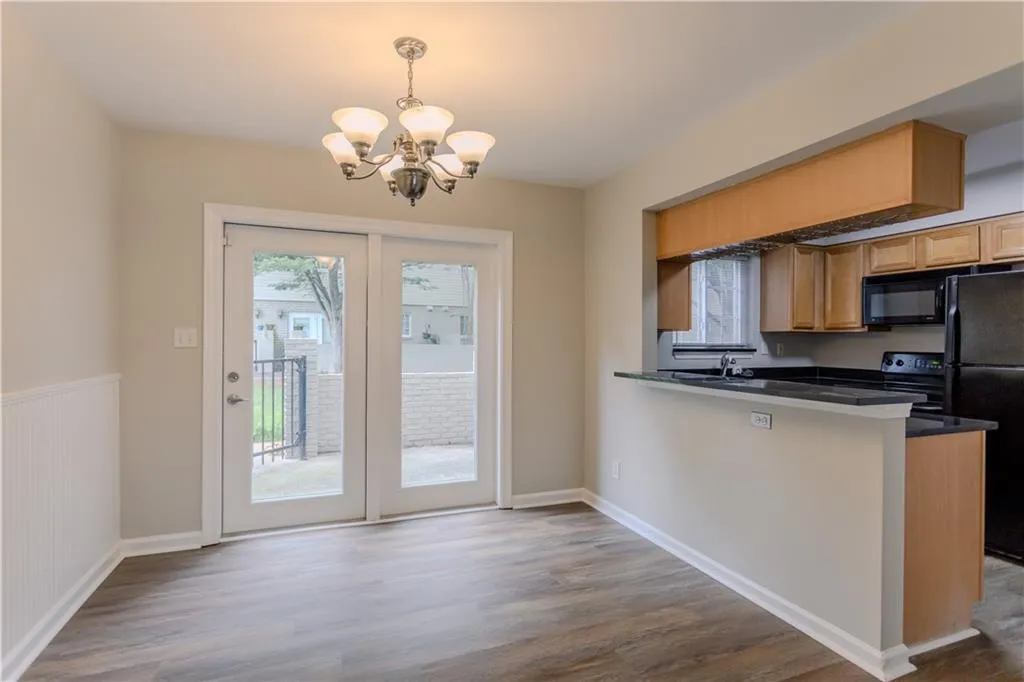 Kitchen featuring dark countertops, a chandelier, black appliances, wood finished floors, and a peninsula