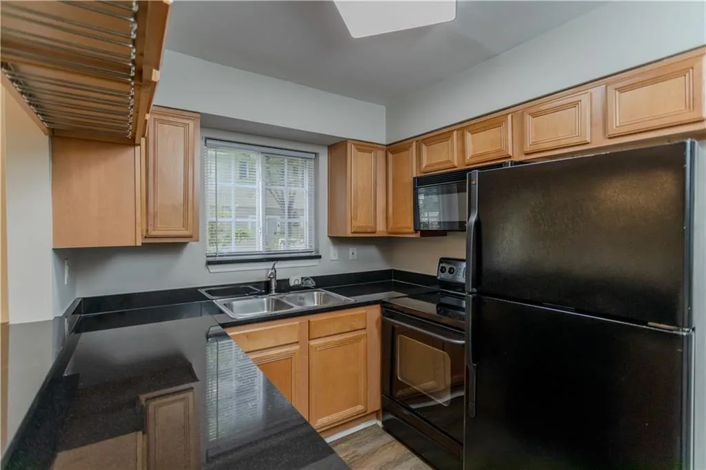 Kitchen featuring black appliances, dark countertops, and light wood-style flooring