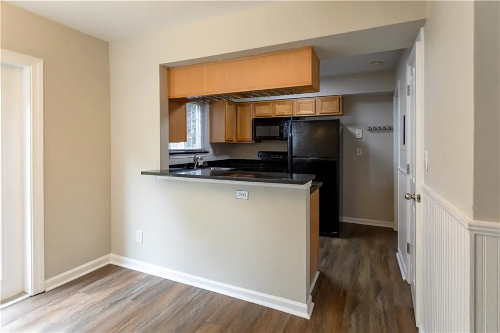 Kitchen with dark countertops, dark wood finished floors, black appliances, a peninsula, and brown cabinetry