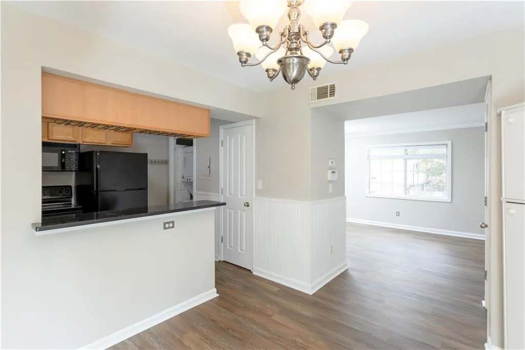 Kitchen featuring a chandelier, dark wood-style flooring, black appliances, dark countertops, and wainscoting