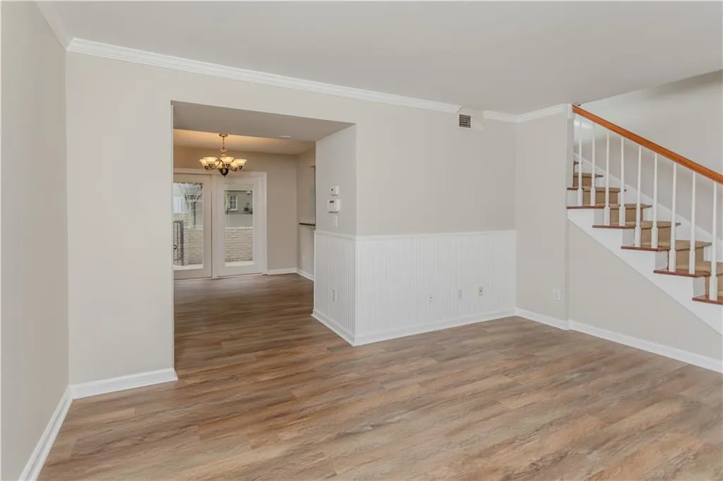 Spare room featuring a chandelier, stairs, wood finished floors, wainscoting, and ornamental molding