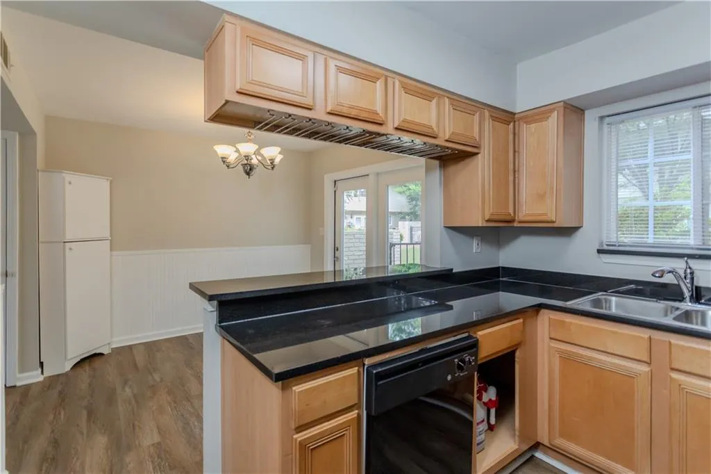 Kitchen with wainscoting, black dishwasher, a peninsula, dark countertops, and wood finished floors