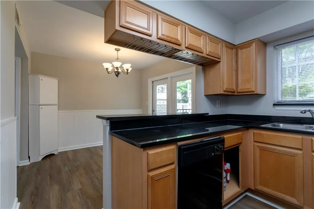 Kitchen with wainscoting, dark wood-type flooring, black dishwasher, dark countertops, and a peninsula