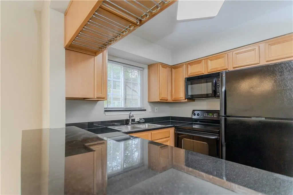 Kitchen with light brown cabinets, black appliances, and dark stone counters