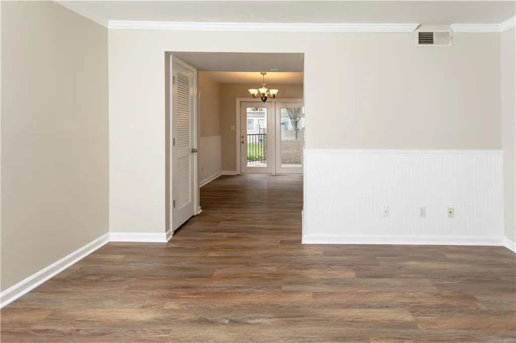 Unfurnished room with crown molding, a chandelier, wood finished floors, and a wainscoted wall