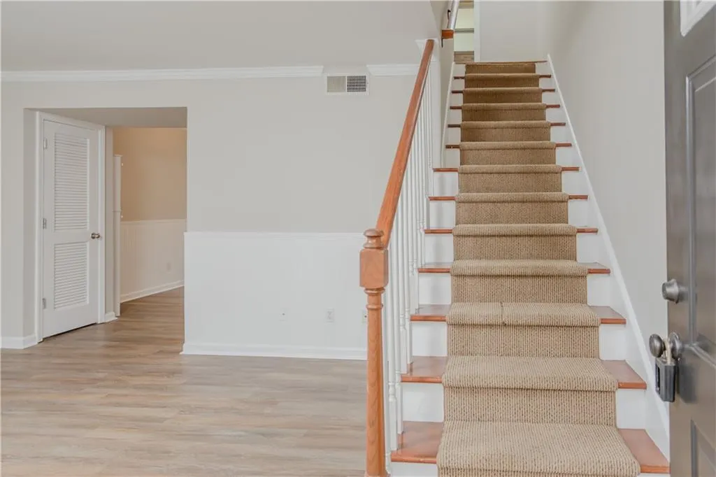 Staircase with wood finished floors, a wainscoted wall, and crown molding