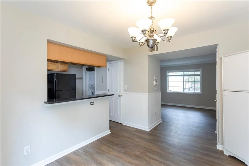 Kitchen featuring a chandelier, freestanding refrigerator, dark wood-style floors, dark countertops, and wainscoting