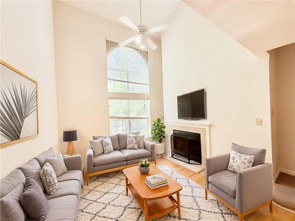 Living area featuring a towering ceiling, wood finished floors, a ceiling fan, and a tiled fireplace